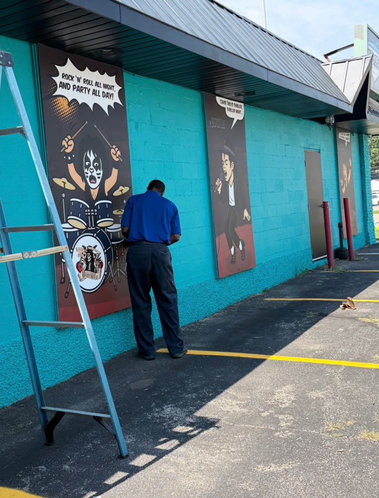 A man painting a mural on a teal building