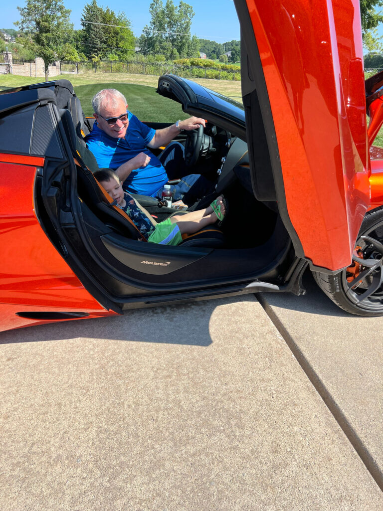 A man in the driver's seat of an orange McLaren with its door raised