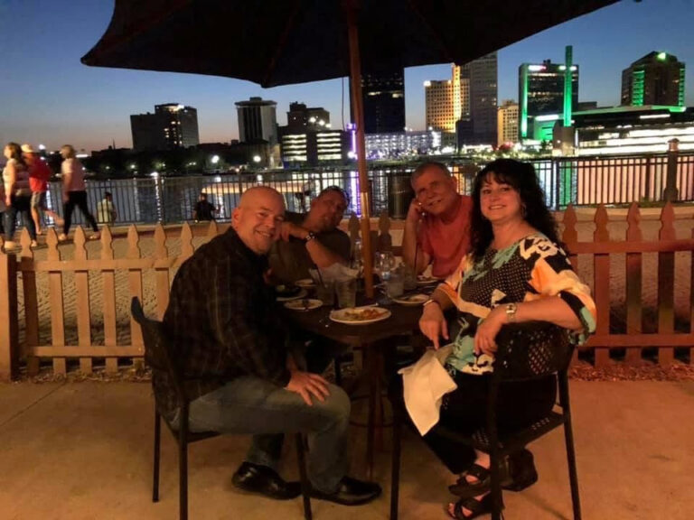 Friends at dinner on a patio with a city skyline at dusk